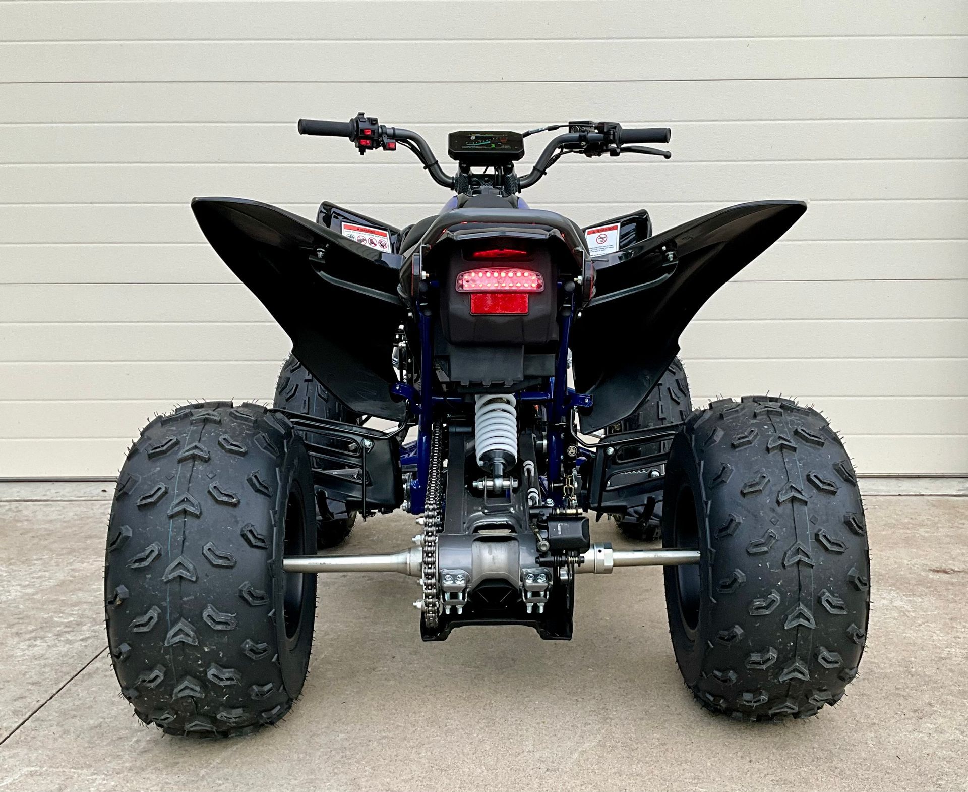 Black sport ATV with oversized knobby tires, viewed from the front against a plain wall.