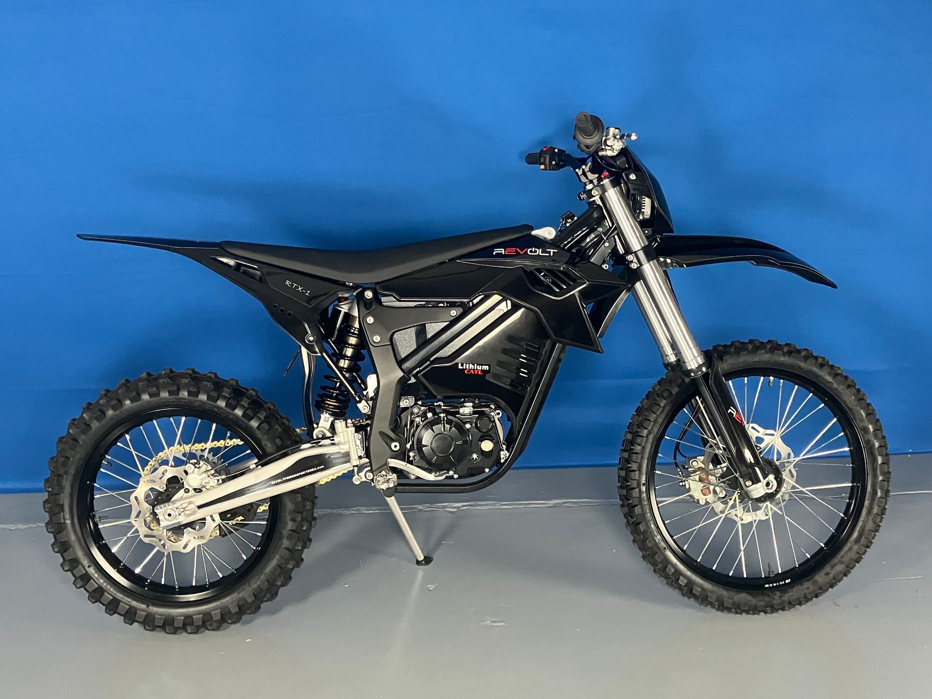 Black off-road dirt bike on a plain blue studio background, side view