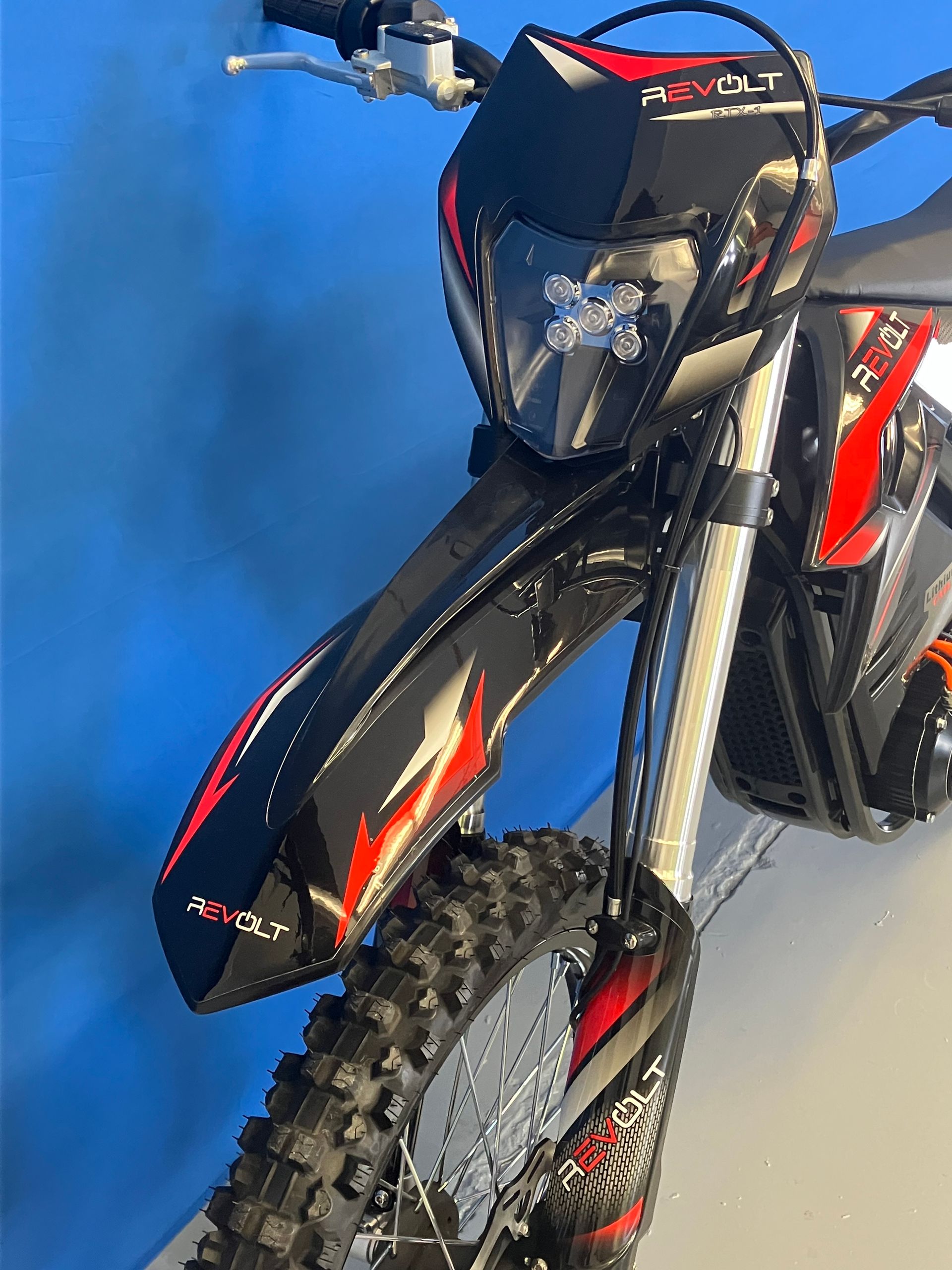 Black and red dirt bike angled against a blue background, showing the front wheel and headlight.