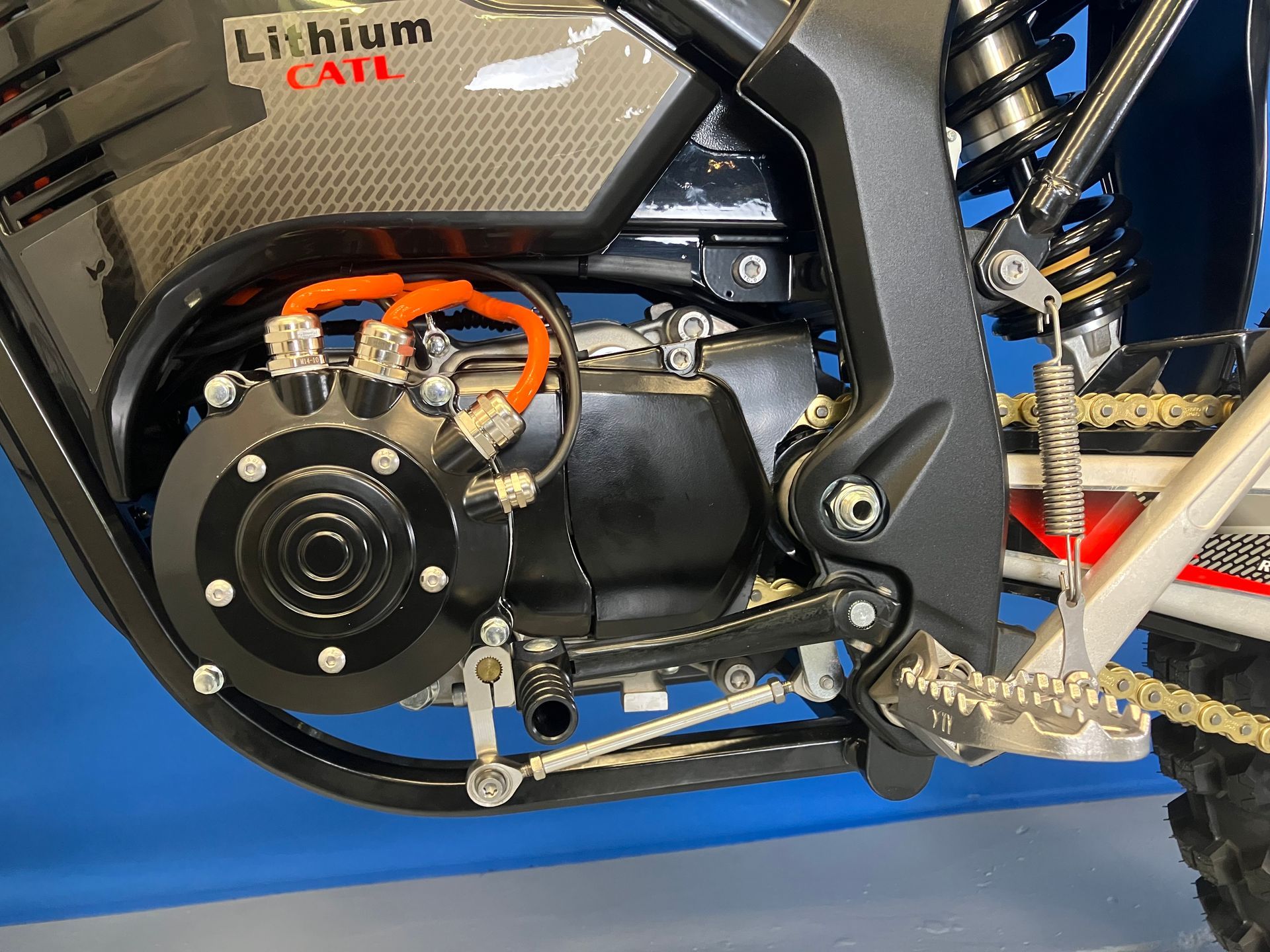Close-up of an e-bike motor and drivetrain with black frame, orange wiring, and silver footpeg.
