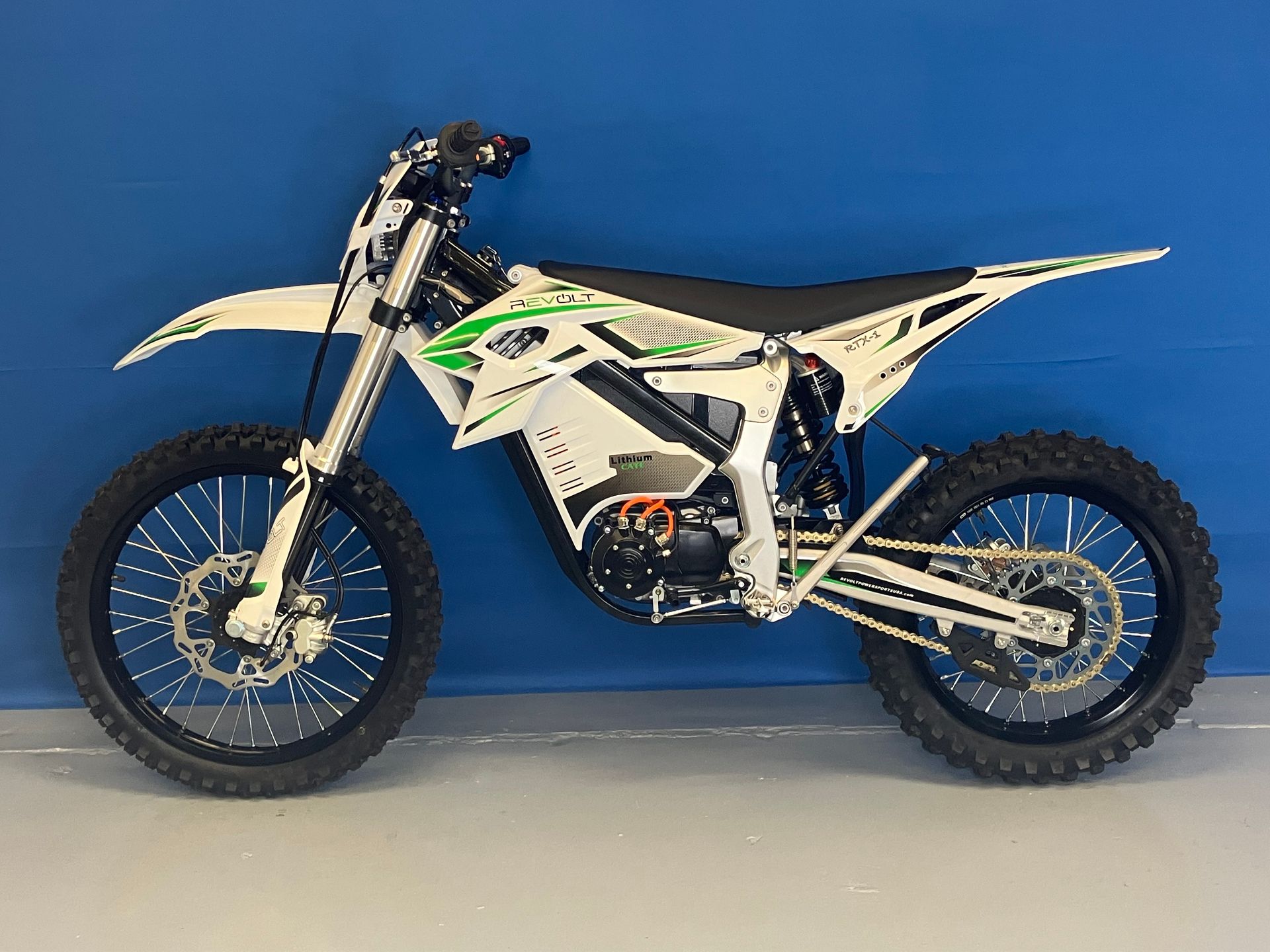White-and-green dirt bike on a gray floor against a blue wall, side view.
