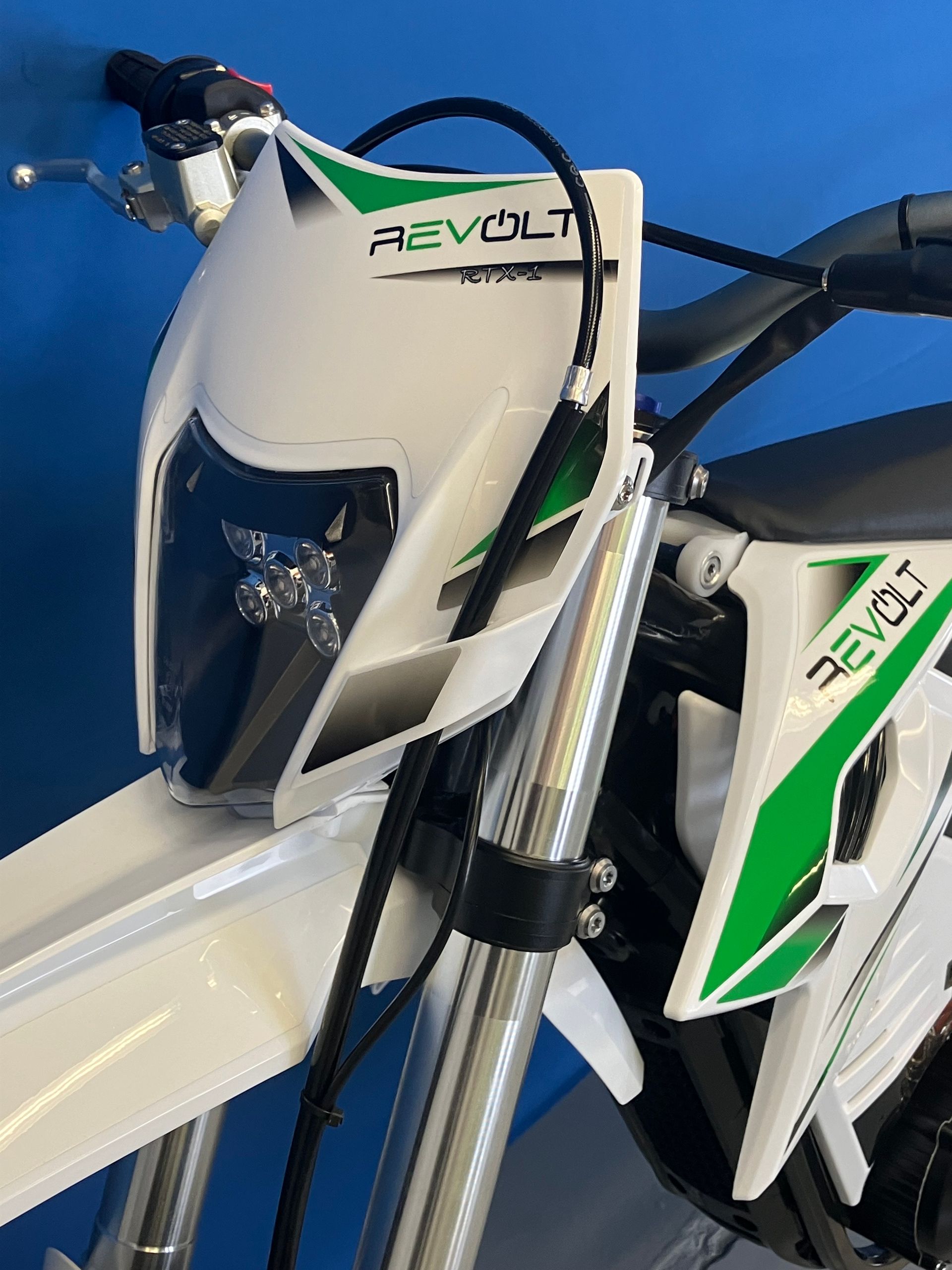 Close-up of a white and green dirt bike with Revolt branding and front suspension visible