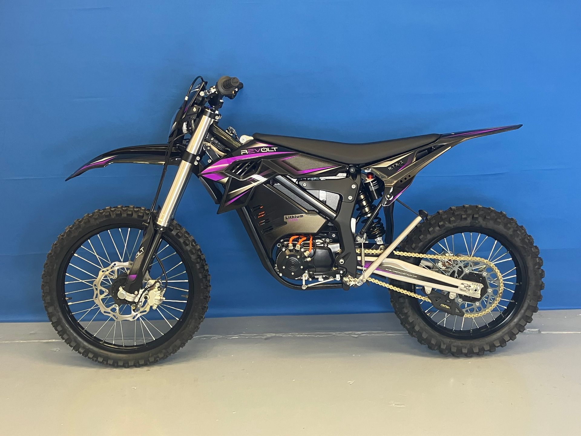 Black and purple dirt bike parked side-on against a blue wall on a concrete floor