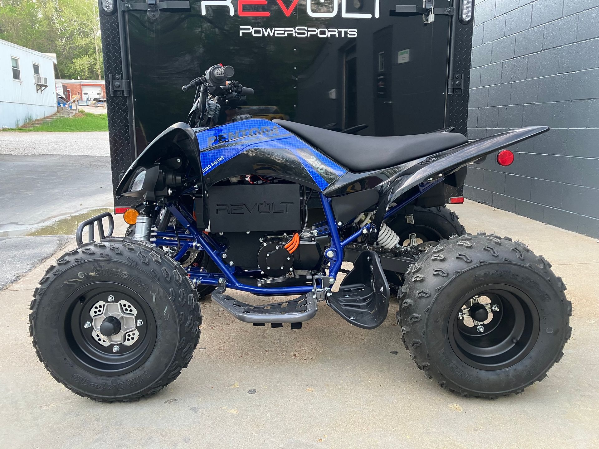 Blue and black ATV parked on pavement in front of a trailer