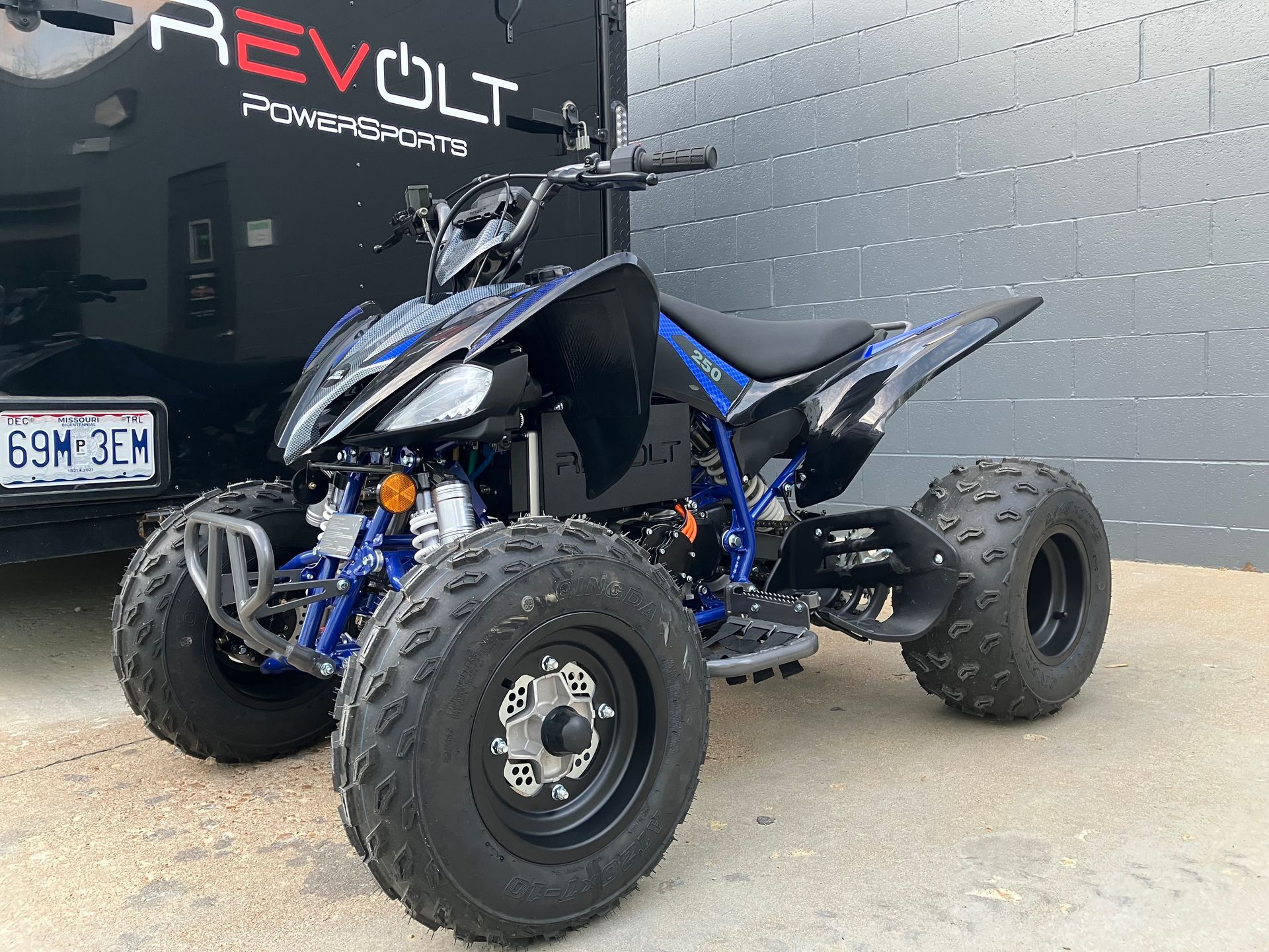 Blue and black ATV parked in front of a Revolt Powersports building