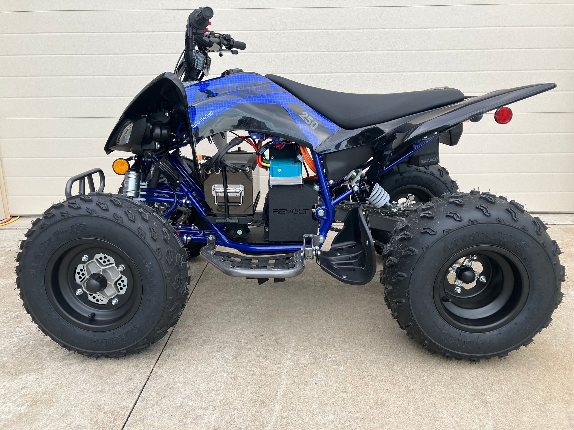 Blue and black ATV with large knobby tires parked on a concrete floor against a white wall.