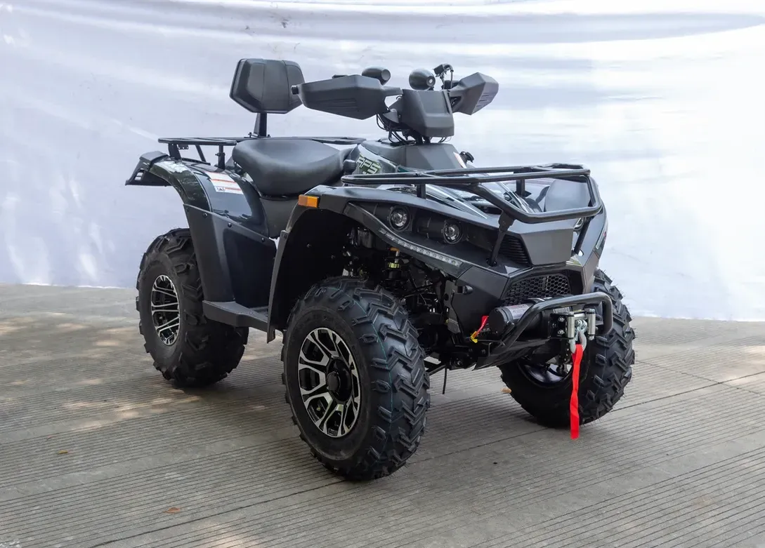 Black ATV with large off-road tires and front winch on a gray floor against a white backdrop
