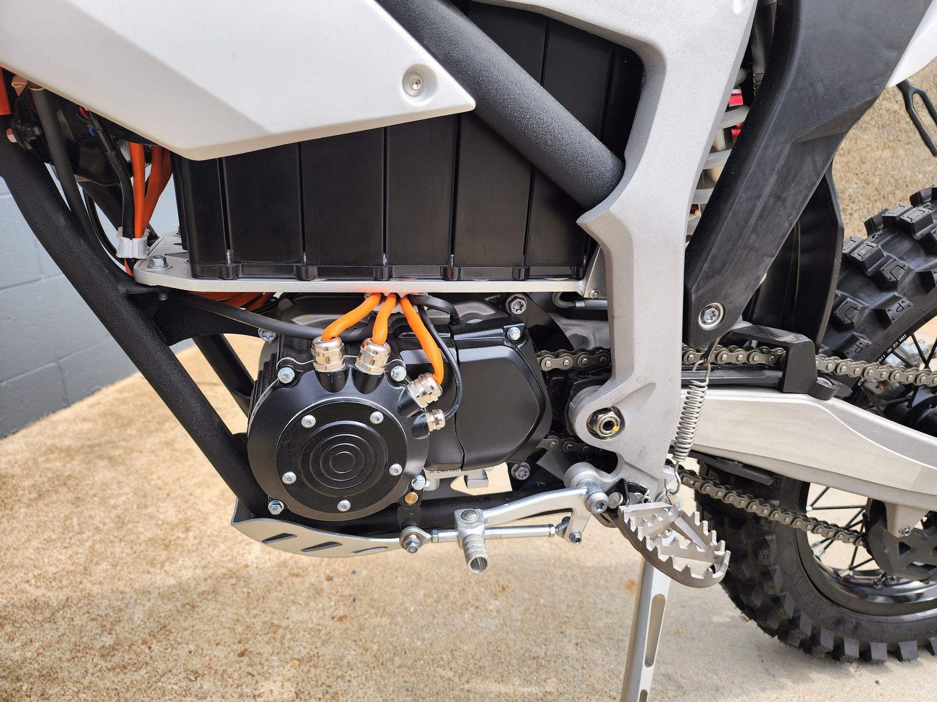 Close-up of a motorcycle engine and foot peg on a dirt bike frame, with black and silver parts