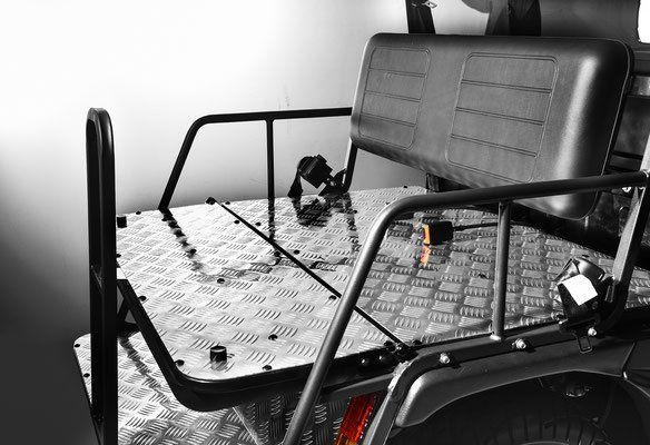Black utility vehicle rear seat with metal cargo rack and diamond-plate floor in a garage.