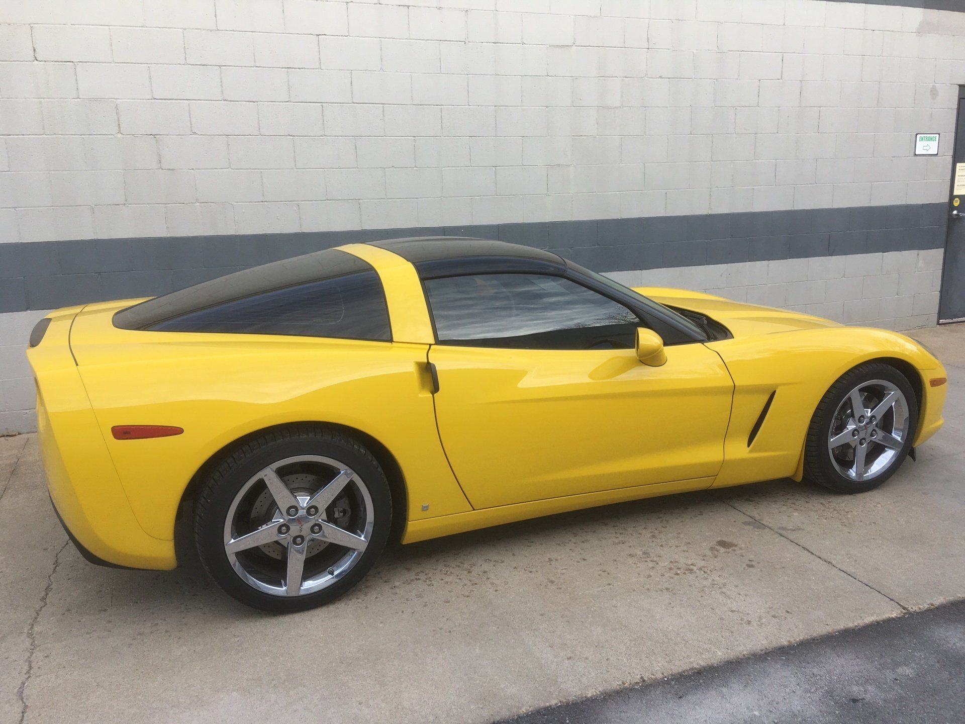 A yellow sports car is parked in front of a brick wall.