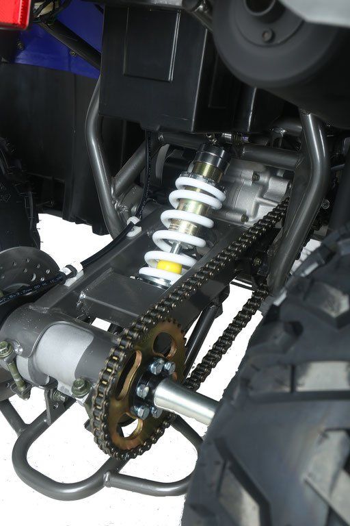 Close-up of a motorcycle rear suspension, chain, and sprocket with a white shock spring.