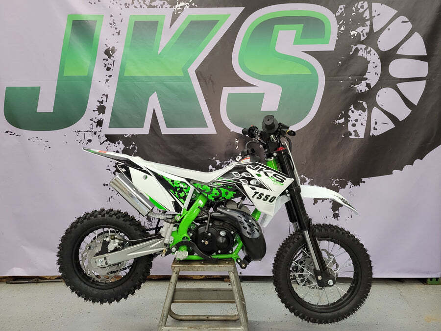 Green and white dirt bike on a stand in front of a JKS backdrop, shown in profile.