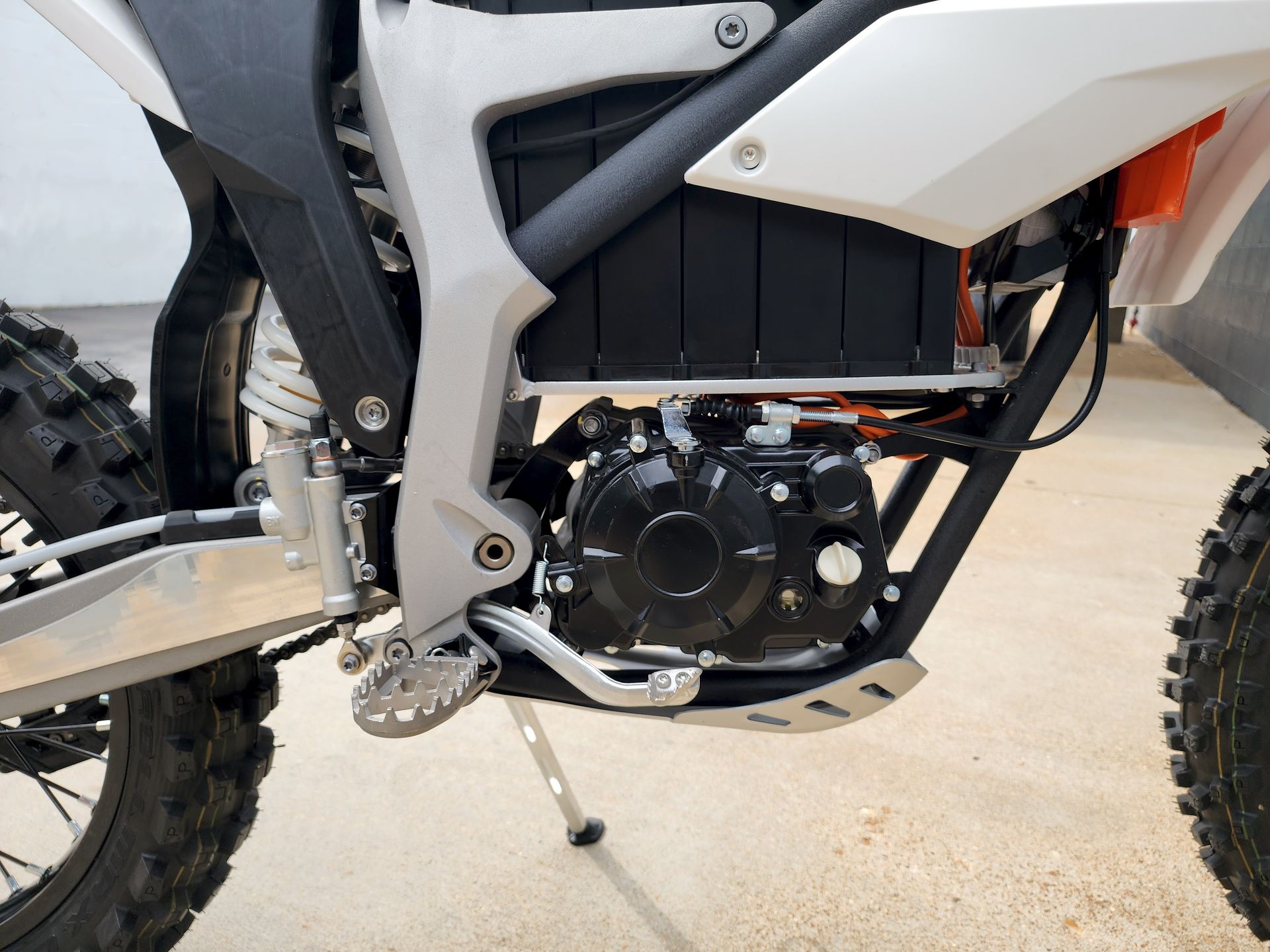 Close-up of a white off-road motorcycle engine and frame on a concrete surface.