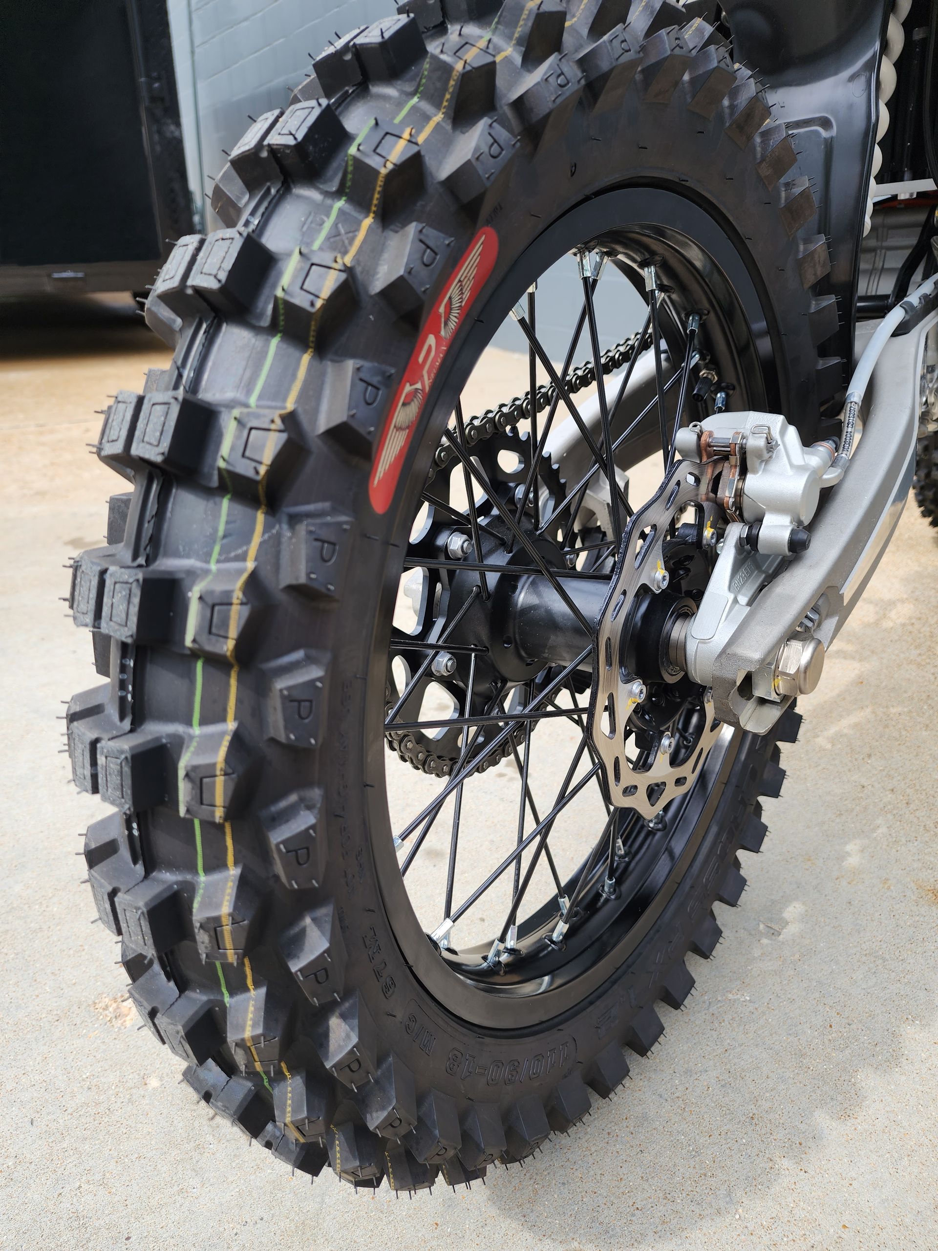 Rear motorcycle wheel with knobby off-road tire on pavement, showing spokes and brake disc