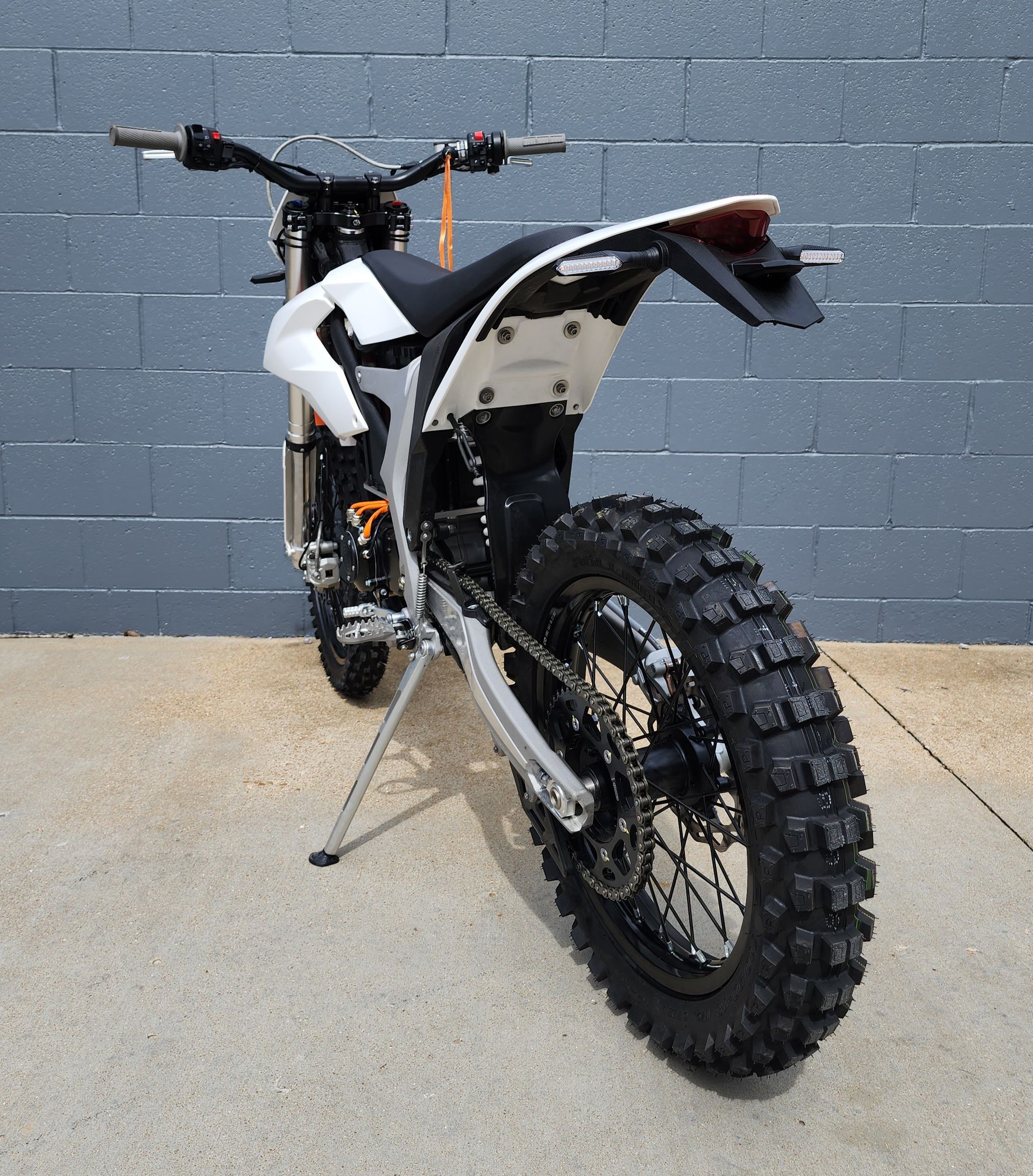 White dirt bike with knobby tires on a stand against a gray wall