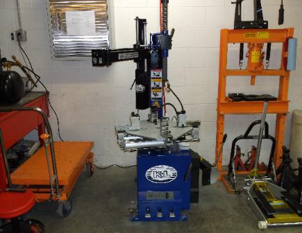 Workshop with a tire-changing machine centered between orange equipment and tool carts.