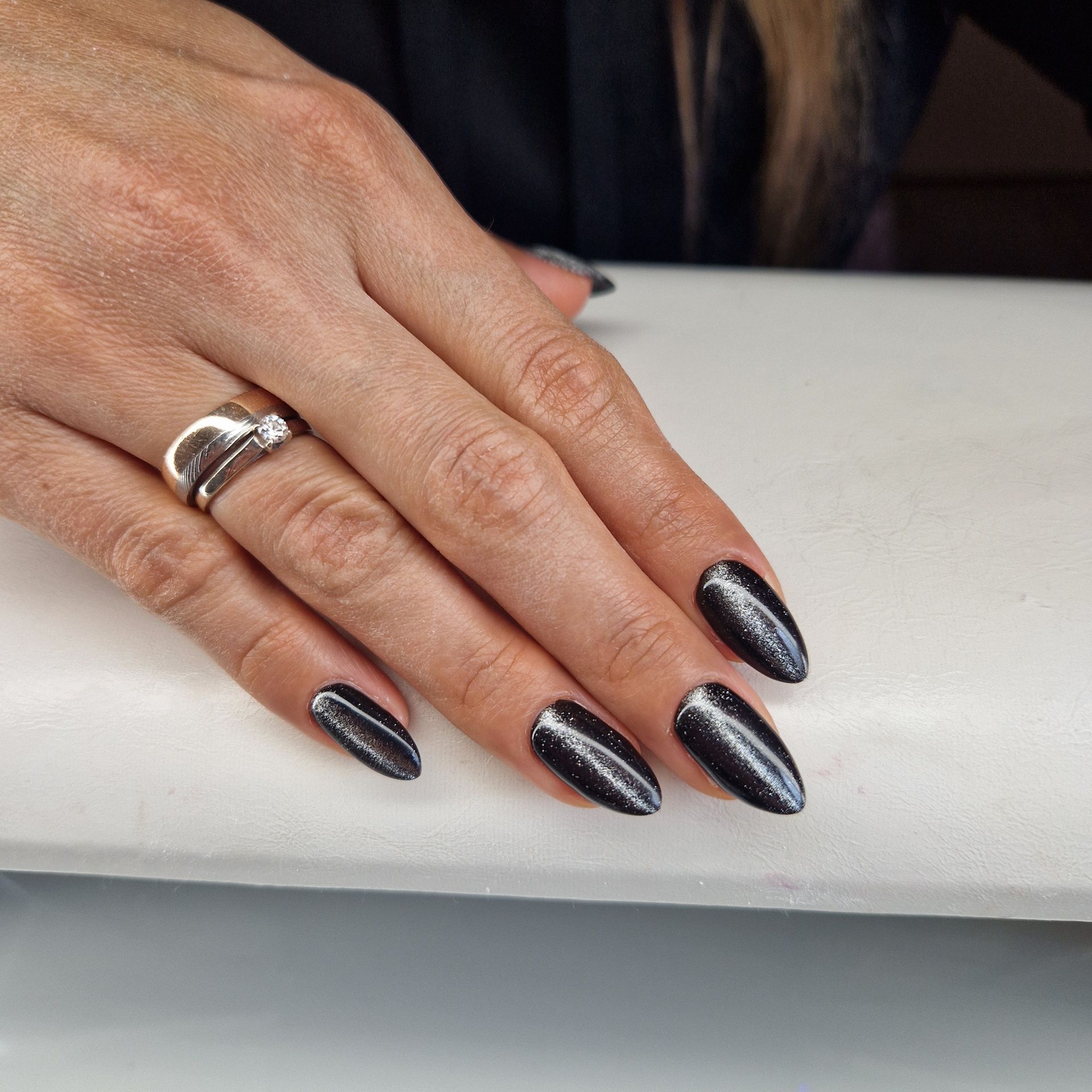 Hand met lange zwarte glitternagels en zilveren ringen, rustend op een witte ondergrond.
