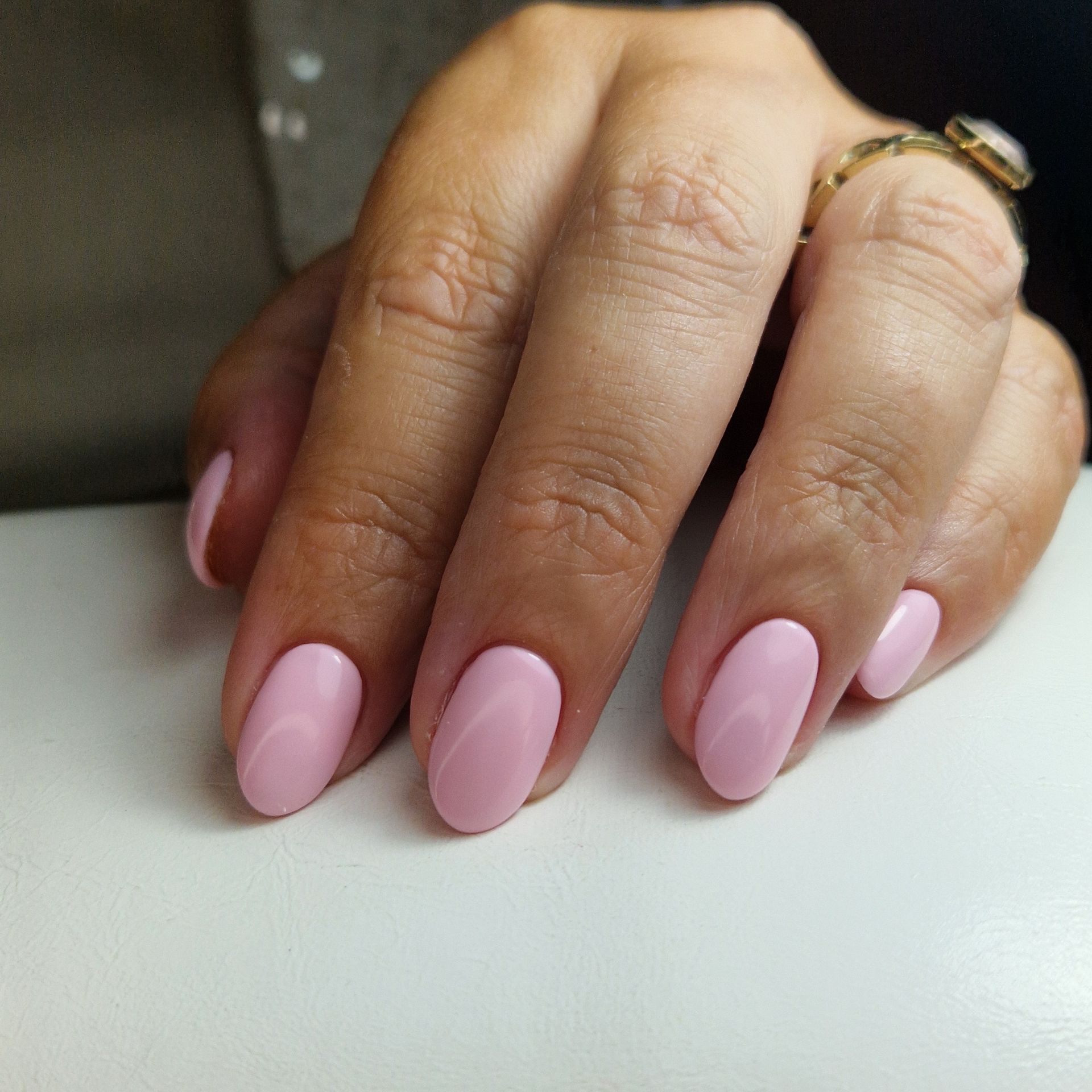 Hand met lichtroze gemanicuurde nagels rustend op een witte ondergrond