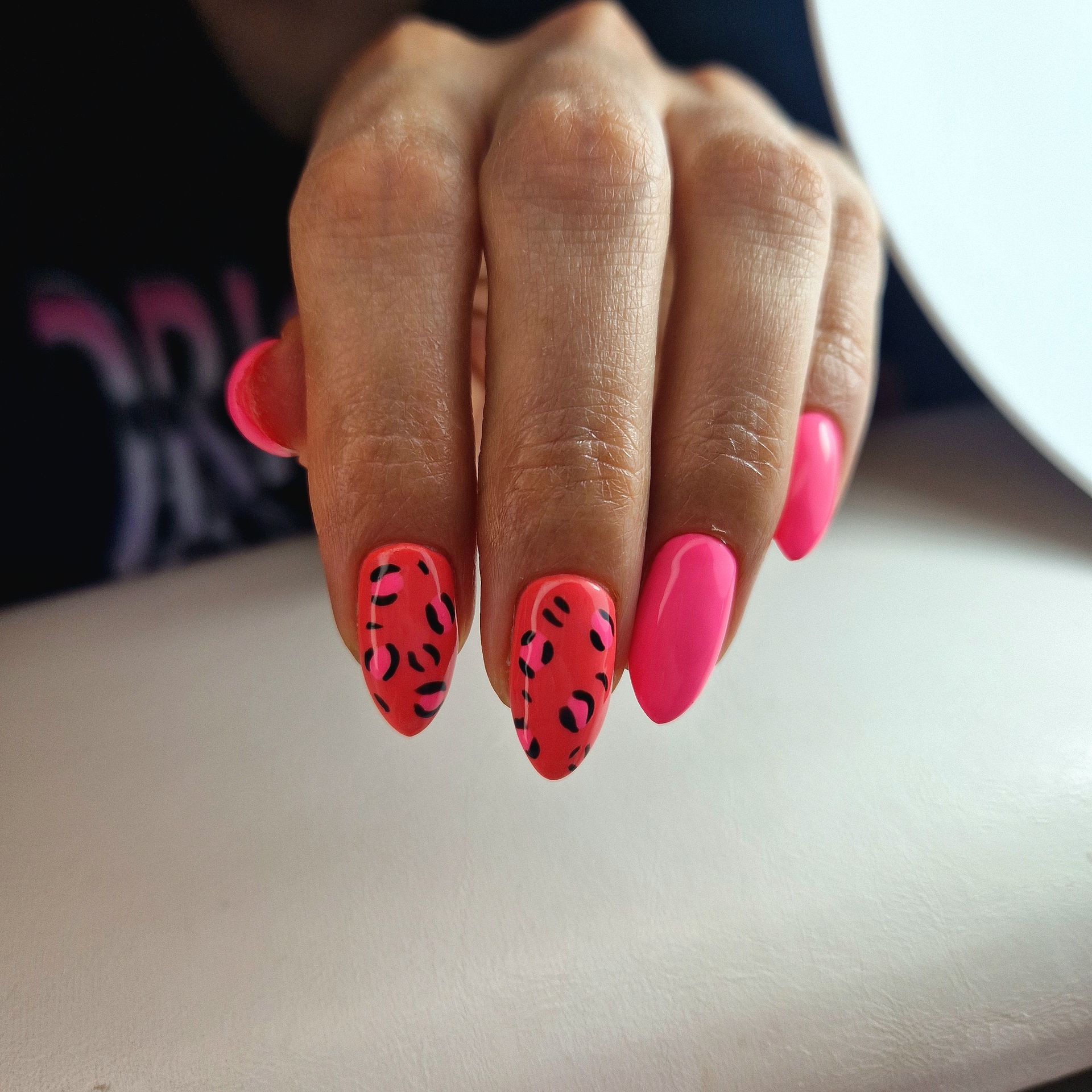 Hand met felroze nagels en accentnagels met panter patroon, rustend op een witte ondergrond.