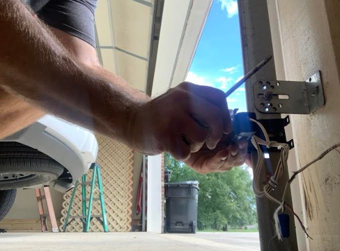 A man is fixing a garage door with a screwdriver.