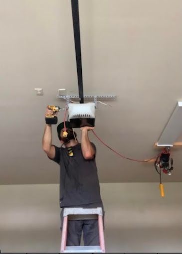 A man is standing on a ladder working on a garage door opener.