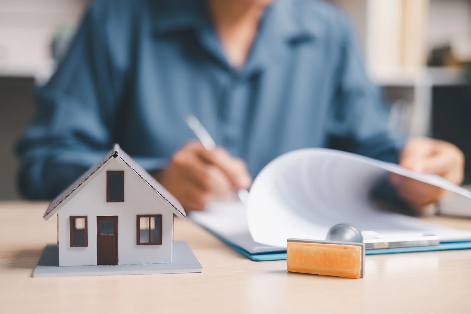 Miniature house and padlock in foreground with a person reviewing documents at a desk