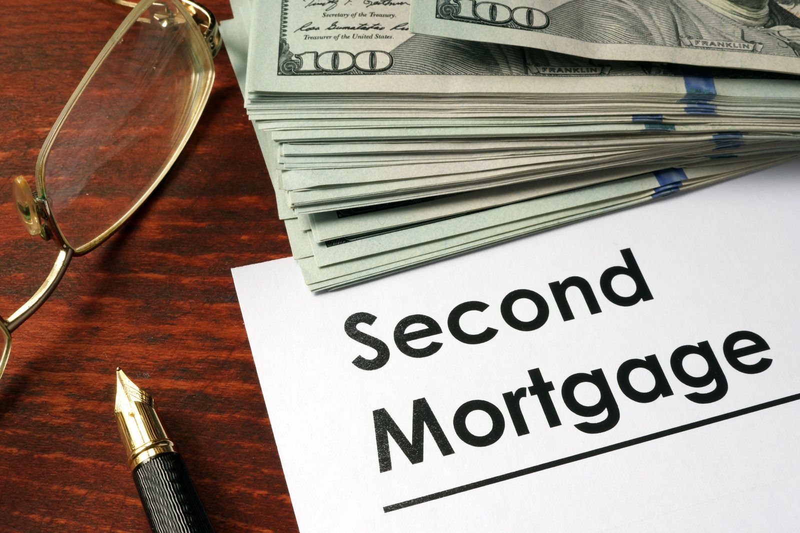 Second Mortgage sign beside stacked dollar bills, pen, and eyeglasses on a desk