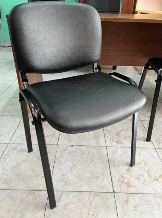 Silla de oficina negra con asiento y respaldo acolchados sobre un suelo de baldosas cerca de un escritorio.
