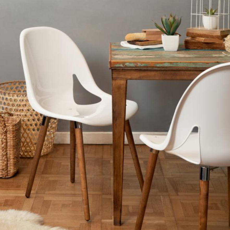 Dos sillas blancas alrededor de una mesa de madera con una planta en maceta en un acogedor rincón de comedor.