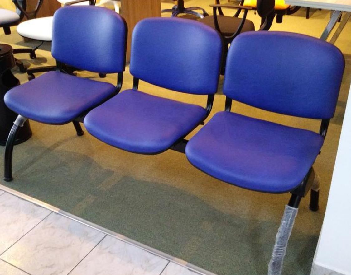Tres sillas de sala de espera tapizadas en azul con patas negras sobre un suelo alfombrado de verde.