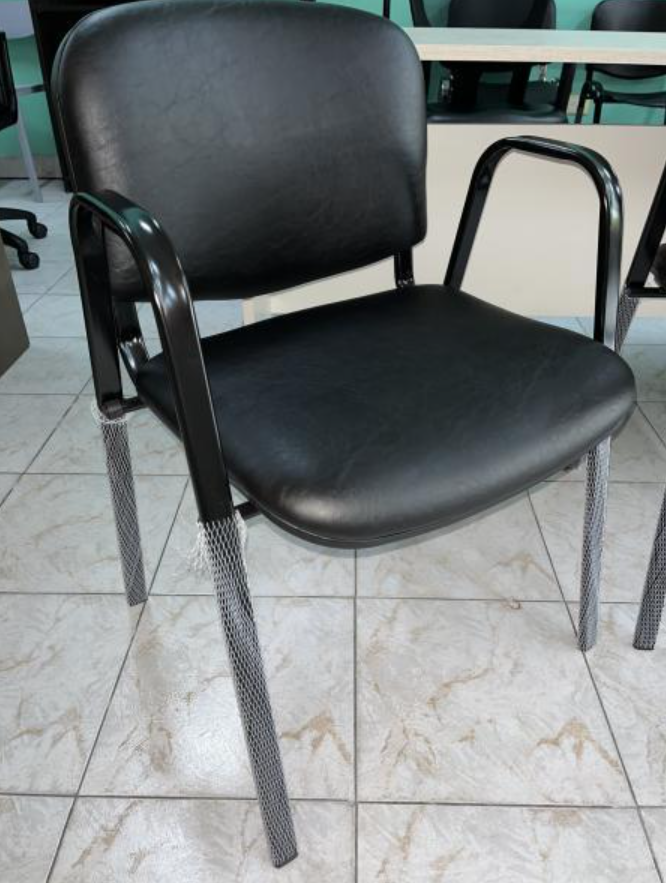 Silla negra acolchada con brazos y patas de metal sobre un suelo de baldosas en el interior.