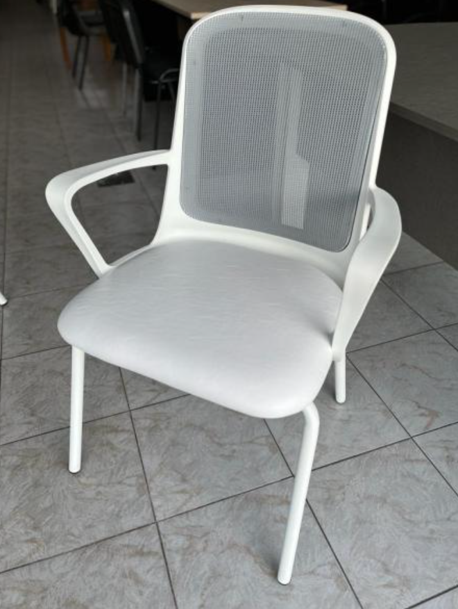 Silla blanca con respaldo de malla y asiento acolchado sobre un suelo de baldosas.