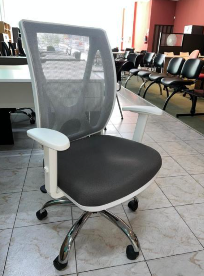 Silla de oficina negra con respaldo de malla, reposabrazos blancos y base cromada en una sala de espera con suelo de baldosas.
