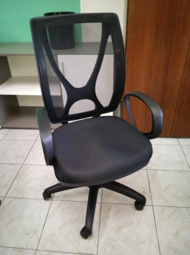 Silla de oficina negra de malla con reposabrazos y ruedas giratorias sobre un suelo de baldosas.