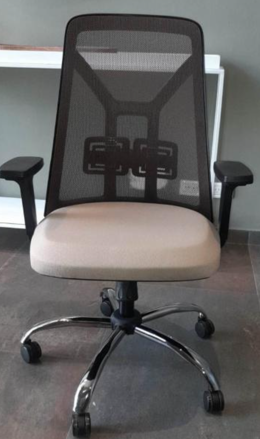 Silla de oficina de malla negra con asiento beige y base cromada con ruedas, apoyada contra una pared clara.