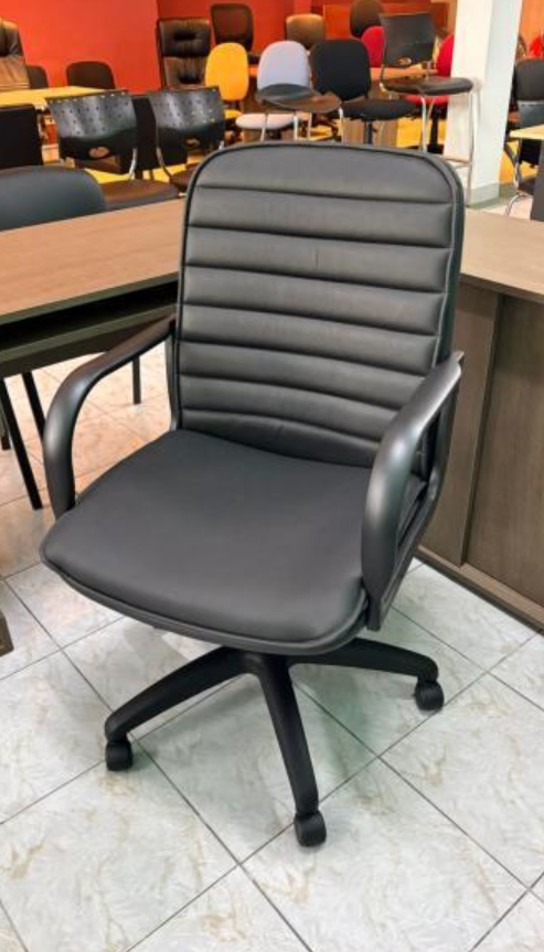 Silla de oficina negra con ruedas en una sala de conferencias cerca de mesas de madera y sillas rojas.