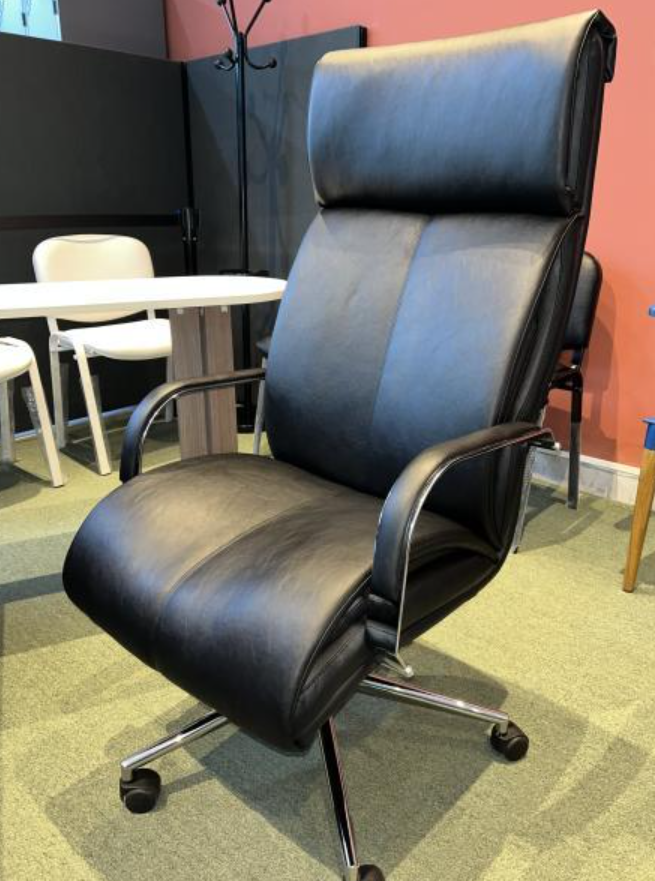 Silla de oficina de cuero negro con ruedas en una habitación moderna con una mesa redonda y sillas blancas cerca.