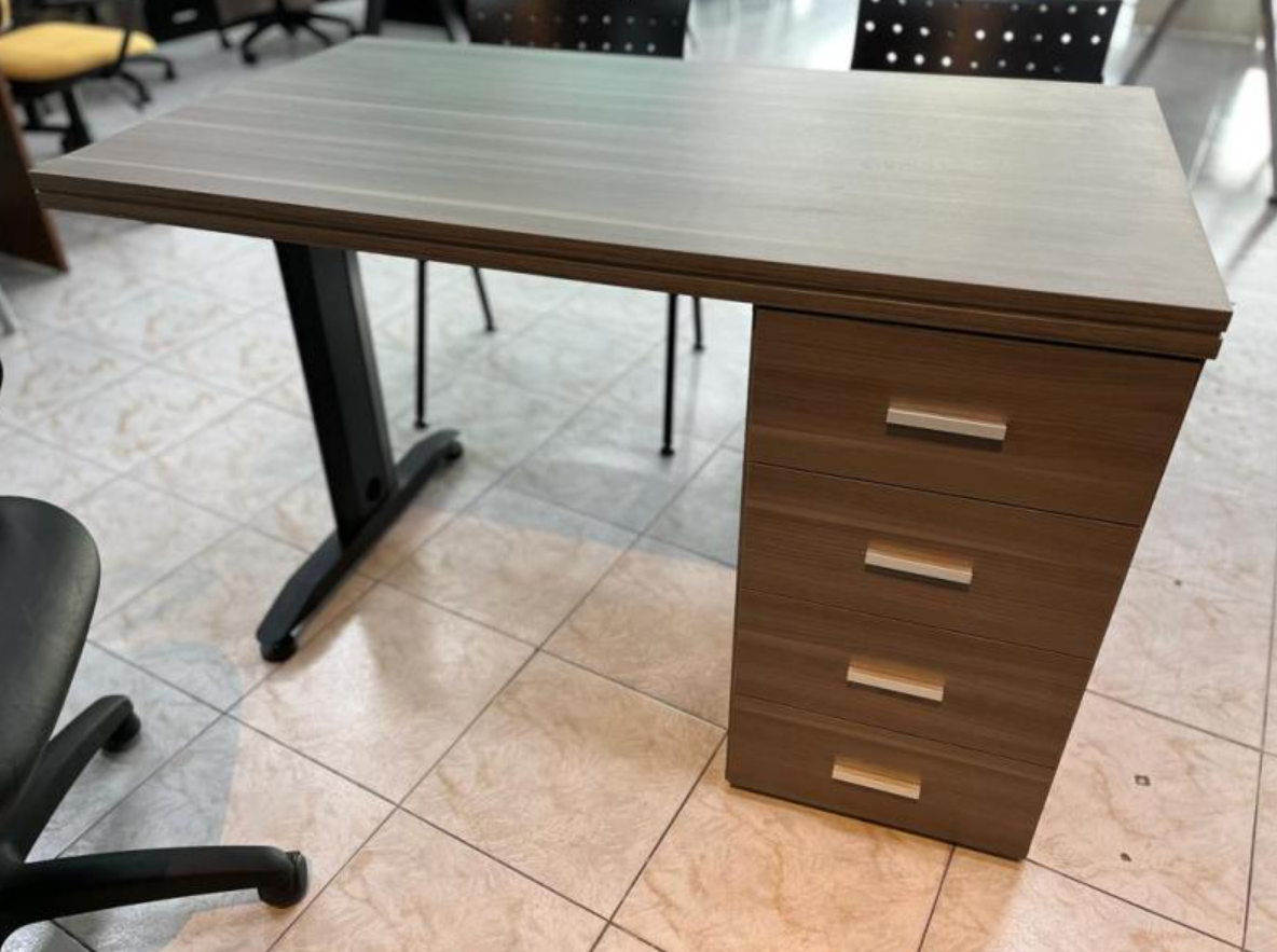 Escritorio de oficina de madera con cajones y patas de metal negro sobre un suelo de baldosas.