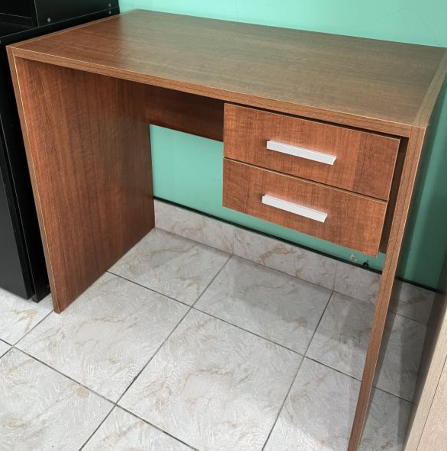 Escritorio de madera con dos cajones, contra una pared verde menta sobre un suelo de baldosas.