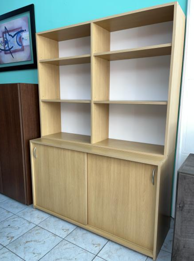 Vitrina de madera clara con estantes abiertos y puertas correderas contra una pared alicatada.