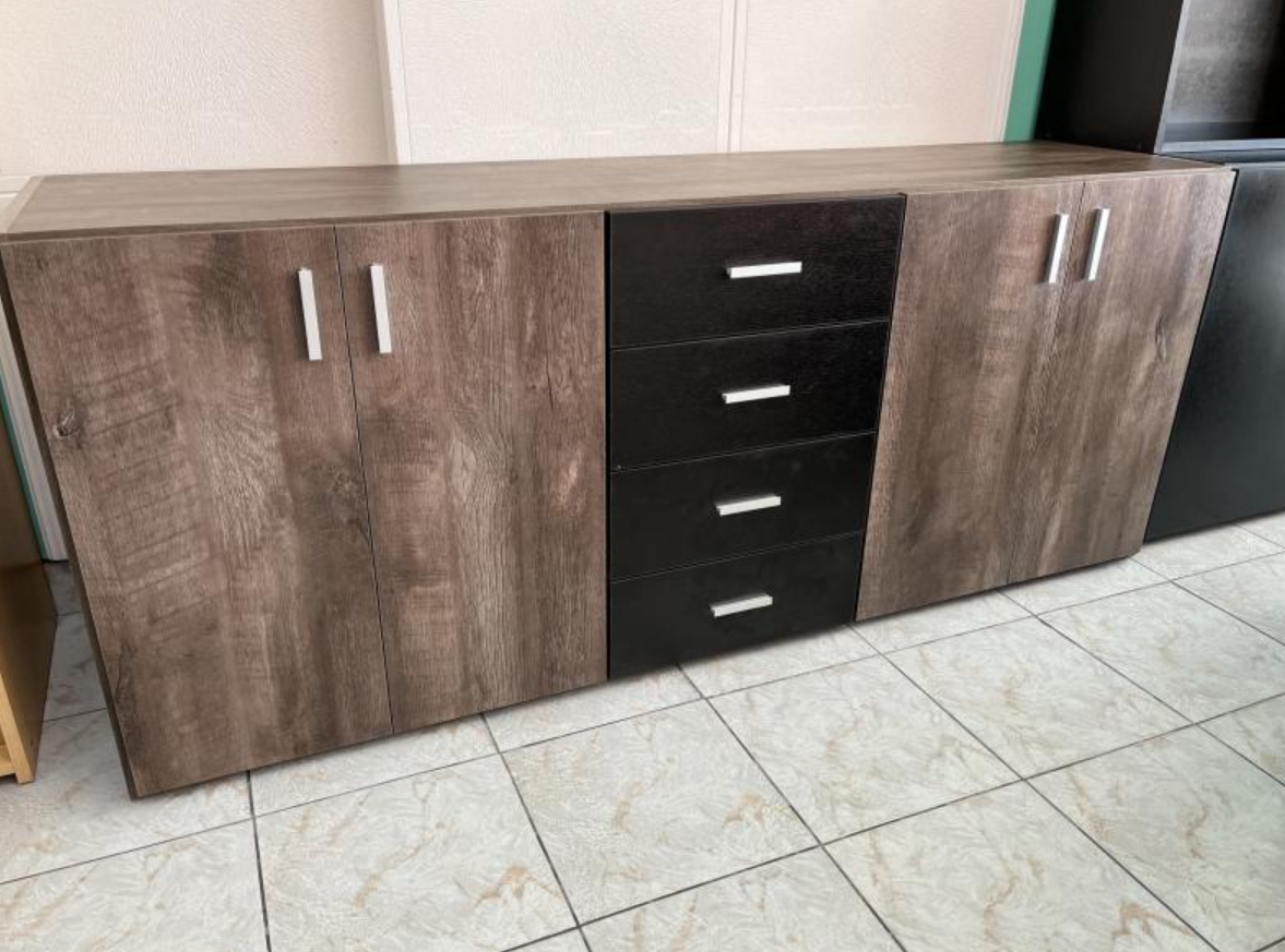 Aparador con acabado de madera, dos armarios y tres cajones centrales sobre suelo de baldosas.