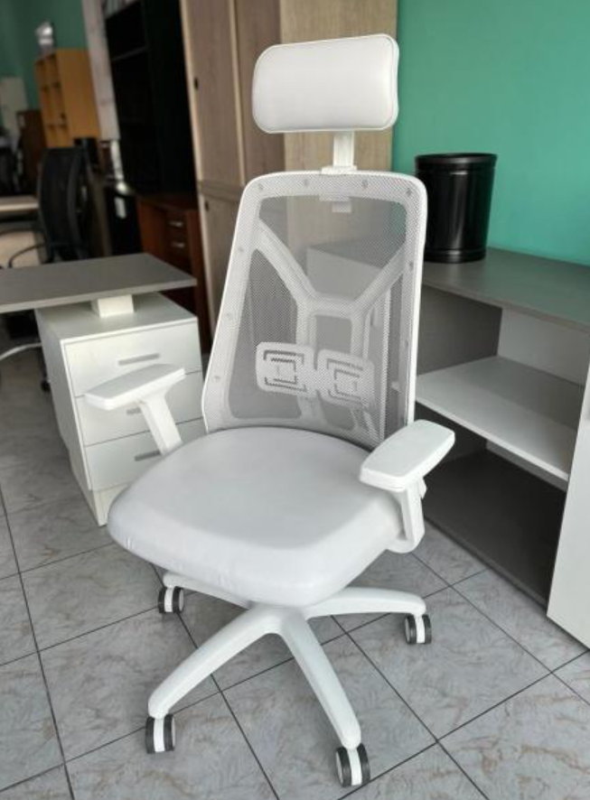 Silla de oficina ergonómica blanca con reposacabezas y respaldo de malla en un espacio de trabajo, sobre un suelo de baldosas.