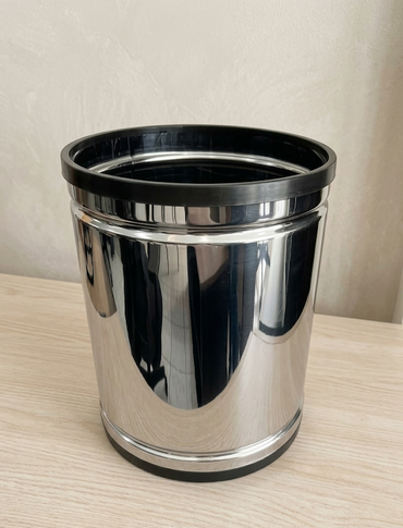 Cubo de basura cilíndrico de acero inoxidable sobre un fondo gris liso.