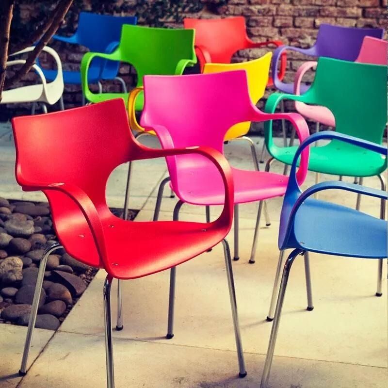 Sillas de colores vivos y brillantes dispuestas al aire libre en un patio, incluyendo asientos rojos, rosas, verdes, azules y amarillos.