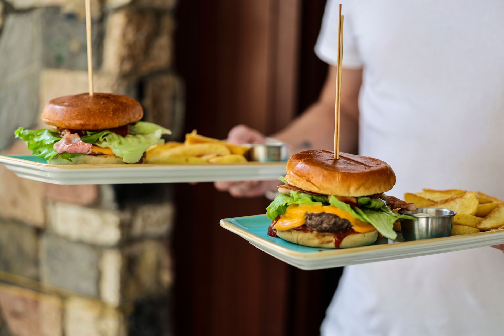 Due hamburger e patatine fritte su vassoi di legno portati all'interno dai camerieri