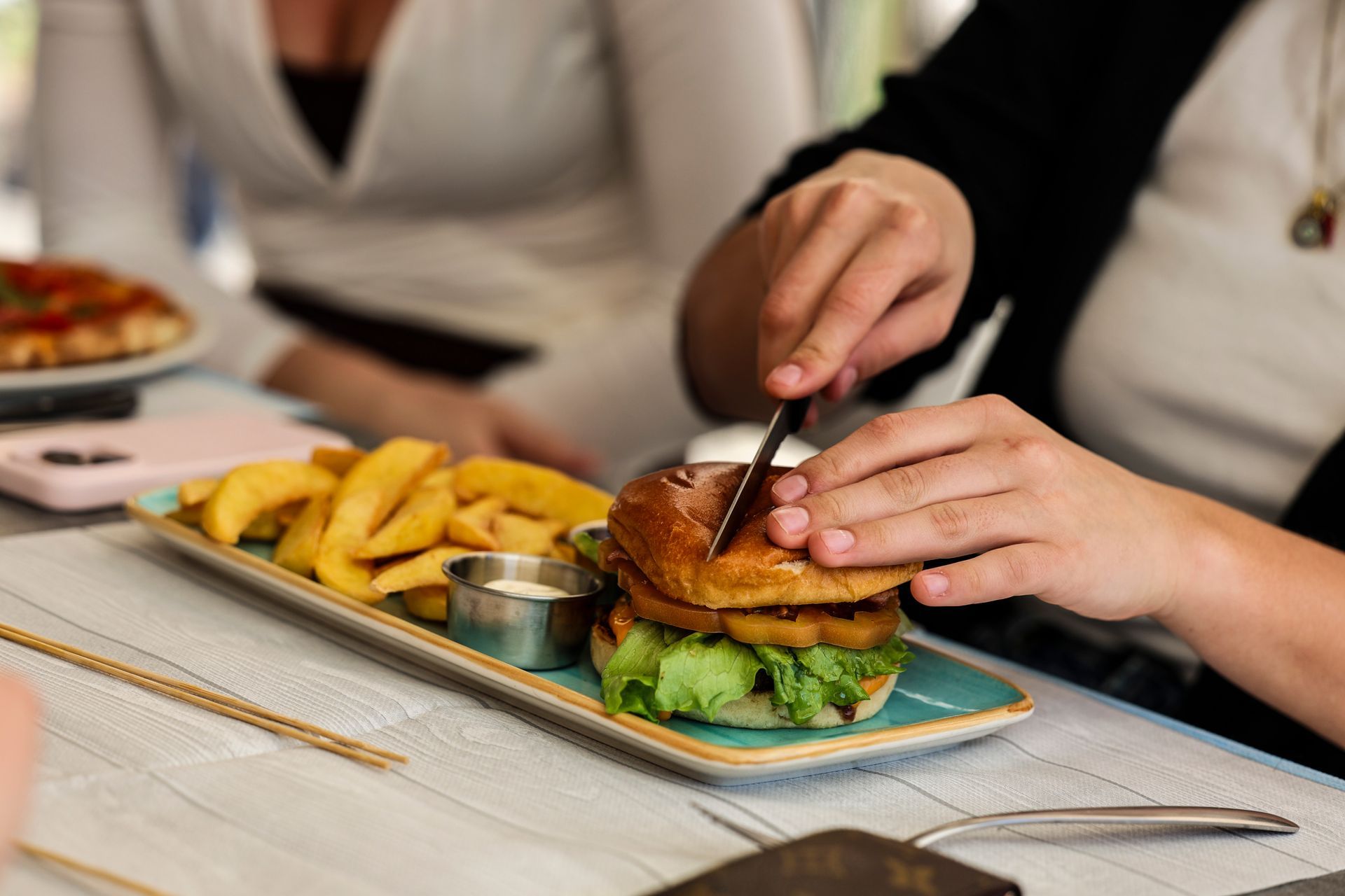 Mani che impiattano un hamburger con patatine fritte su un tavolo di ristorante.
