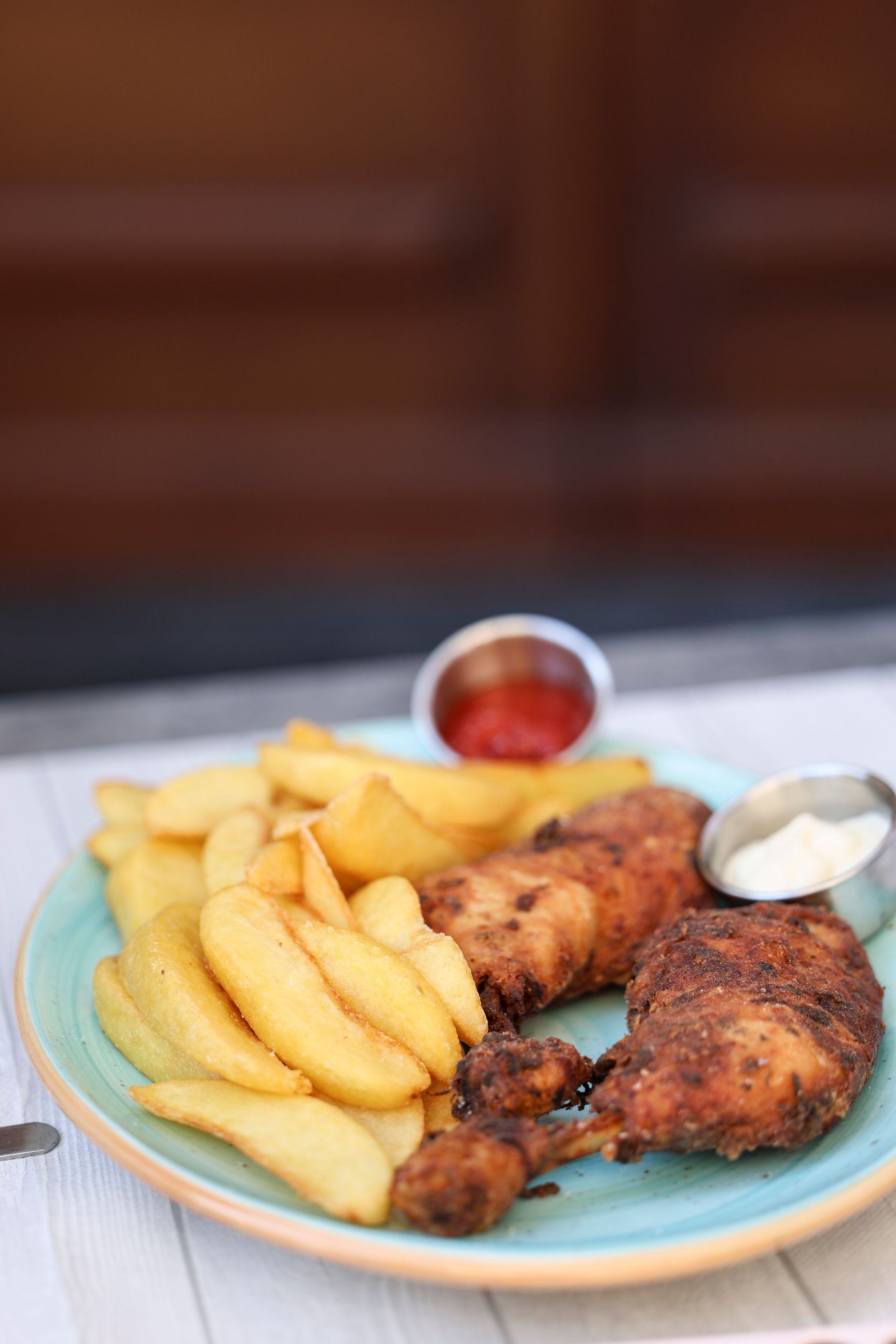 Piatto di cosce di pollo fritte e spicchi di patate con salse, serviti su un piatto blu.
