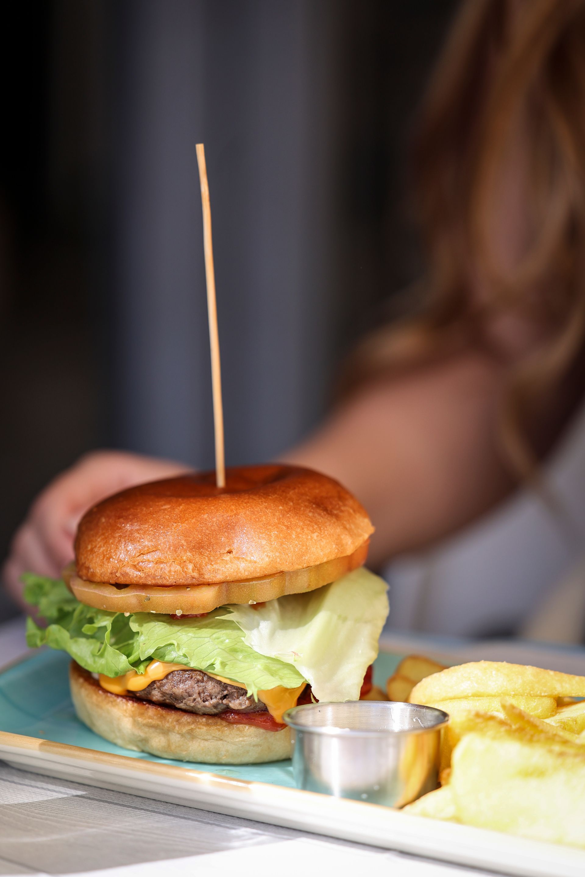 Un hamburger con patatine fritte e salsa è appoggiato su un tavolo, con una mano che si protende verso il pasto.
