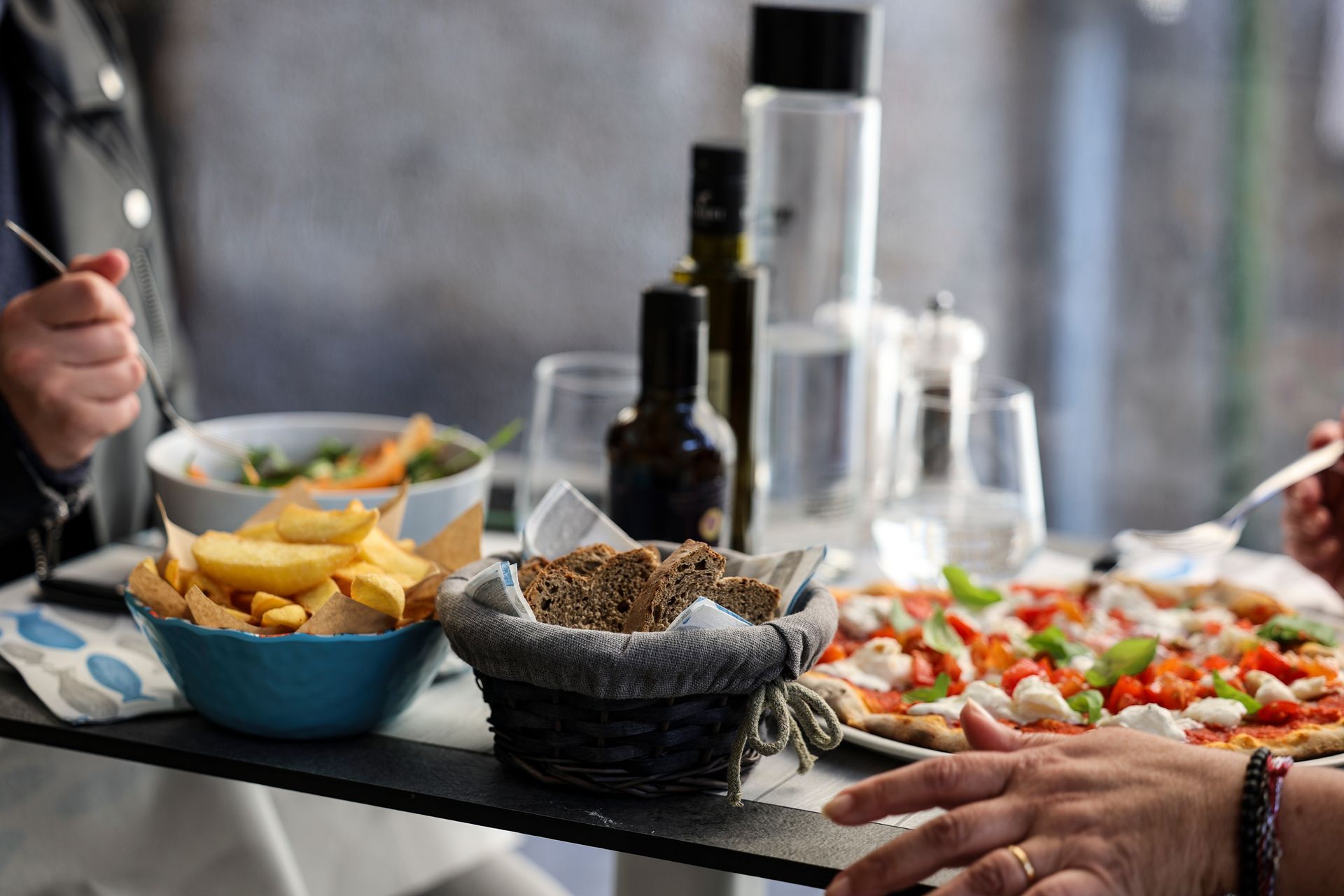 Un tavolo con ciotole di patatine, salsa e un'insalata colorata durante un pasto, con mani che si allungano per prenderle.