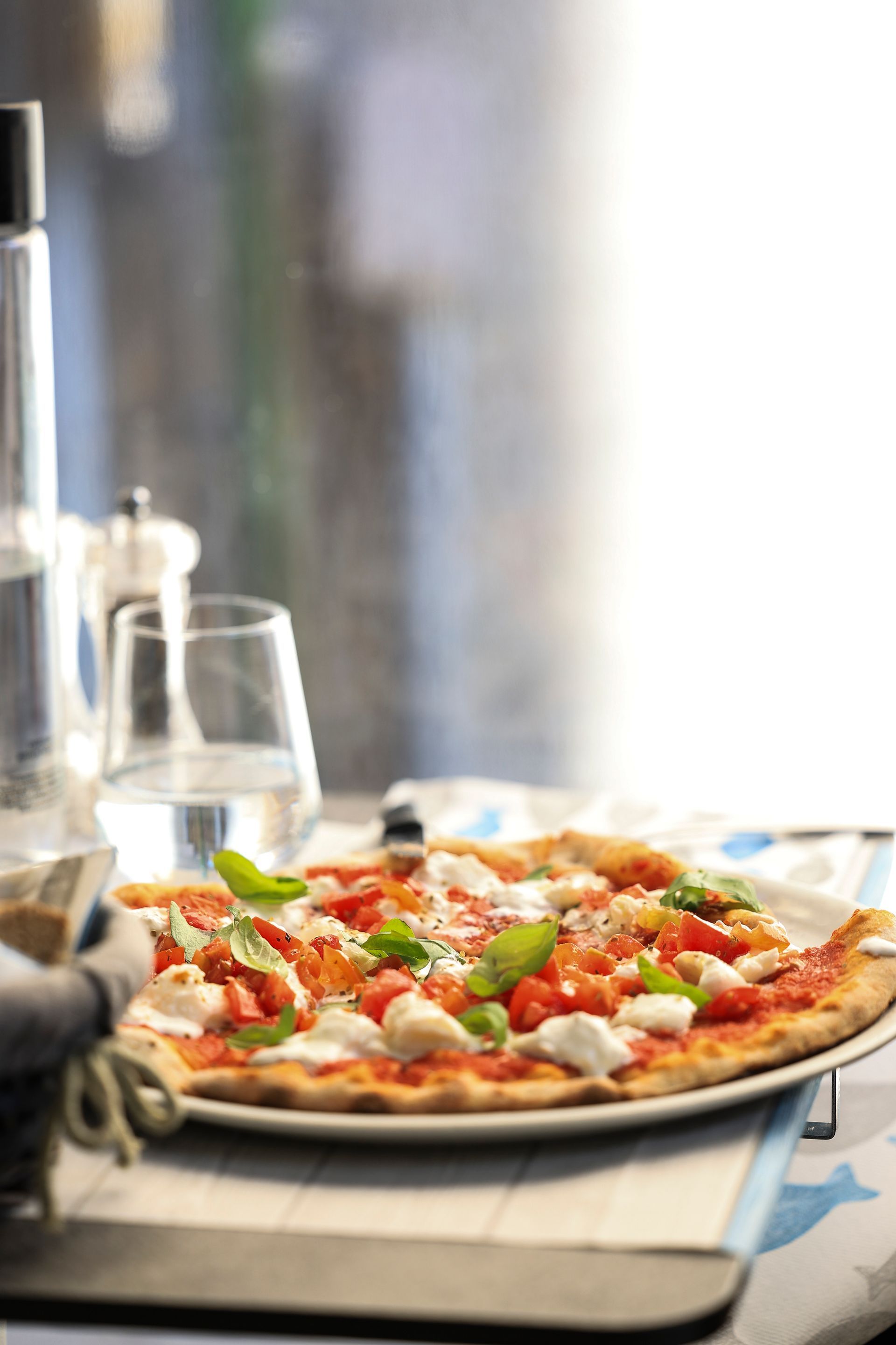Pizza condita con basilico e pomodori su un tavolo di ristorante con un bicchiere d'acqua